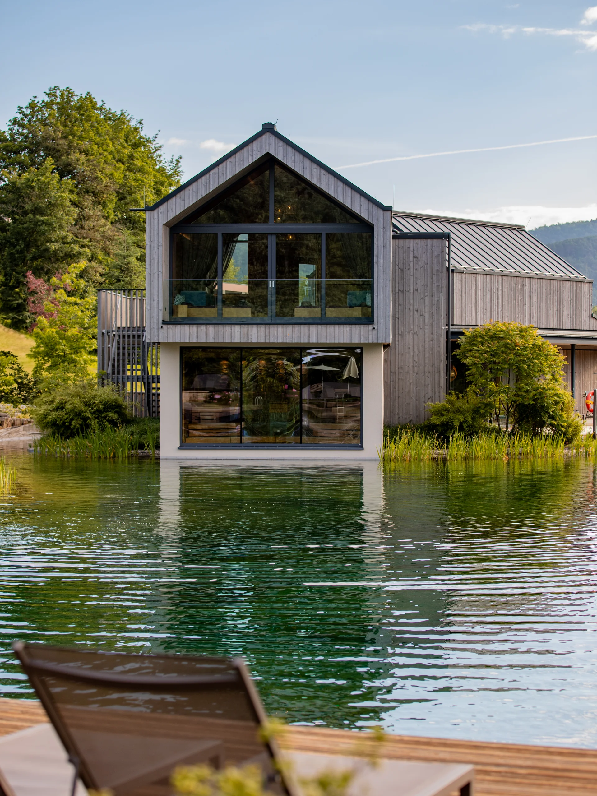 Modernes Haus mit großen Fenstern am ruhigen See umgeben von Natur