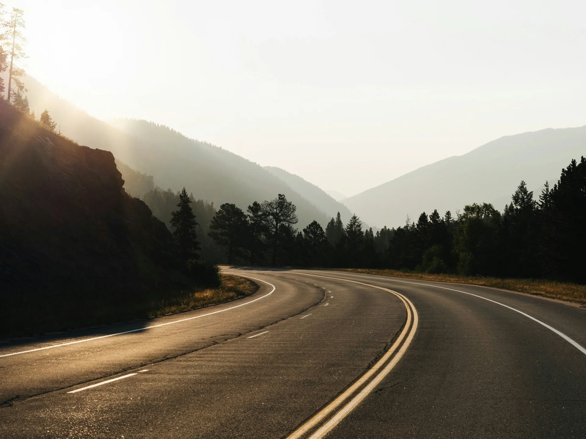 Route vide en courbe au lever du soleil dans un paysage montagneux