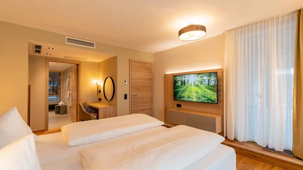 Modernes Hotelzimmer mit Doppelbett, TV und Schreibtisch neben offenem Bad