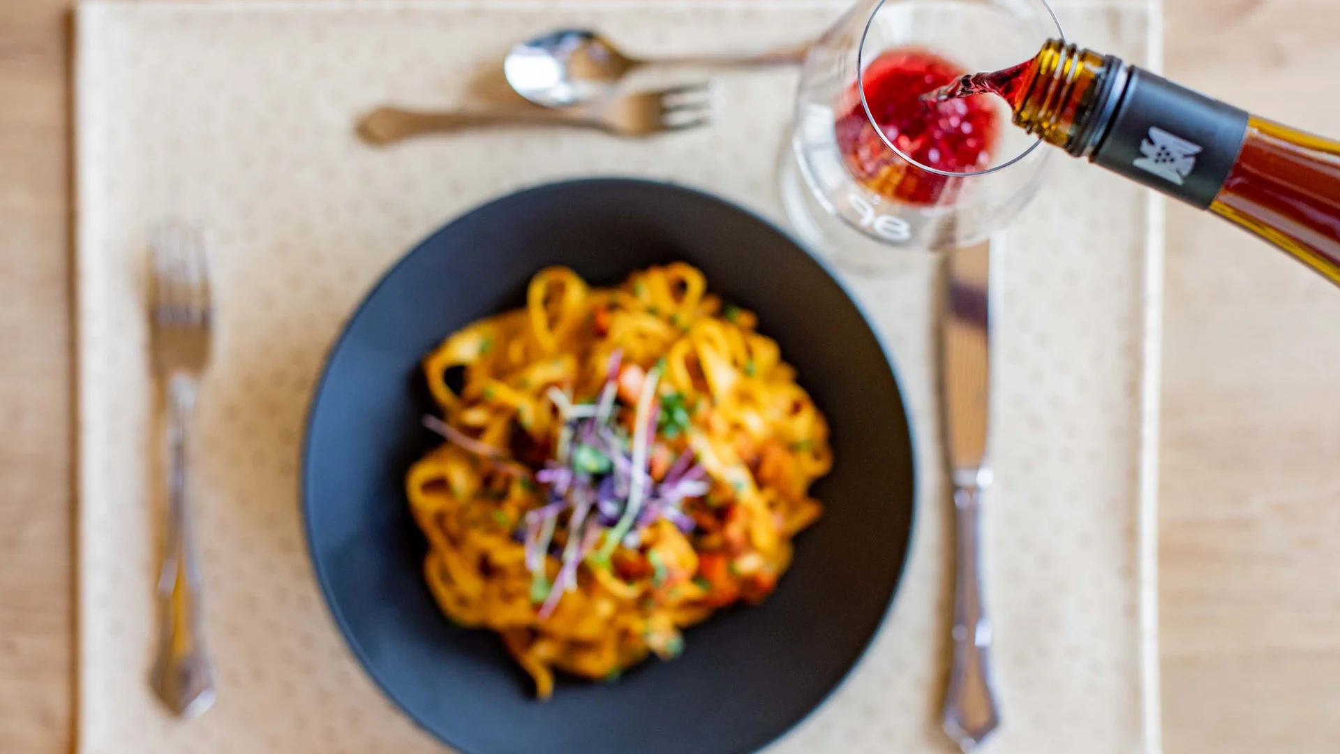 Pasta auf schwarzem Teller und roter Wein wird in Glas eingeschenkt