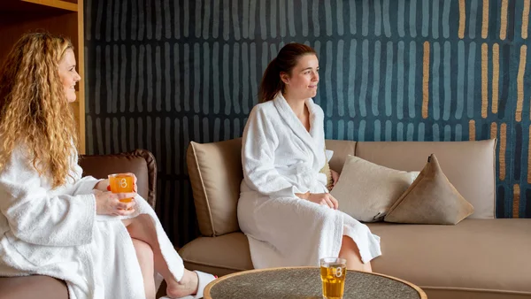 Zwei Frauen in Bademänteln sitzen und trinken Saft in einem gemütlichen Raum