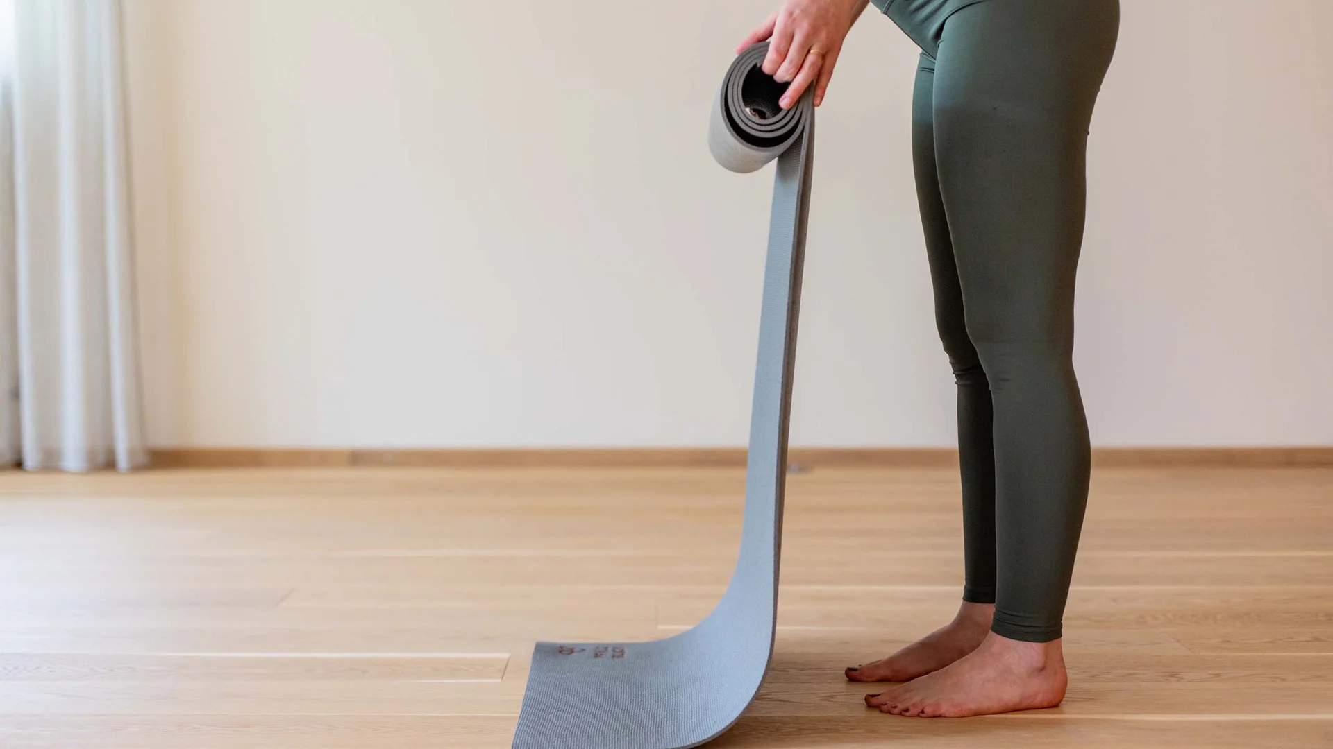 Person rollt eine graue Yogamatte auf Holzboden auf