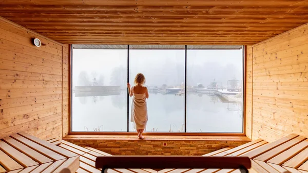 Frau in Handtuch blickt aus Sauna auf nebligen See