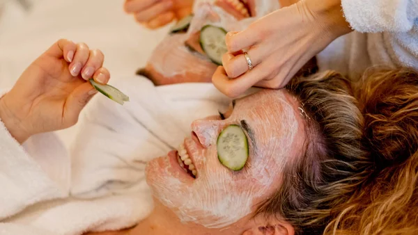 Zwei Frauen mit Gesichtsmasken und Gurkenscheiben auf den Augen im Bademantel
