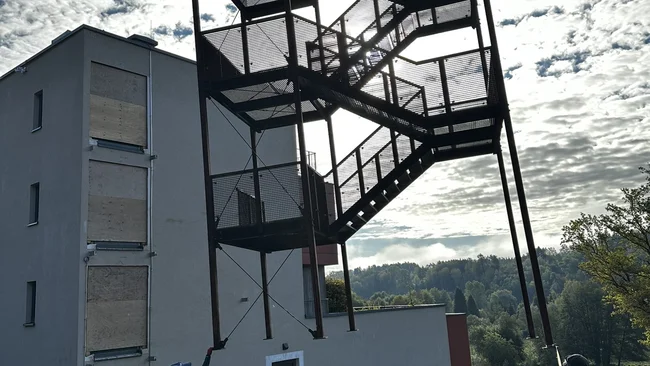 Une tour d’escalier en acier est positionnée par une grue devant un bâtiment