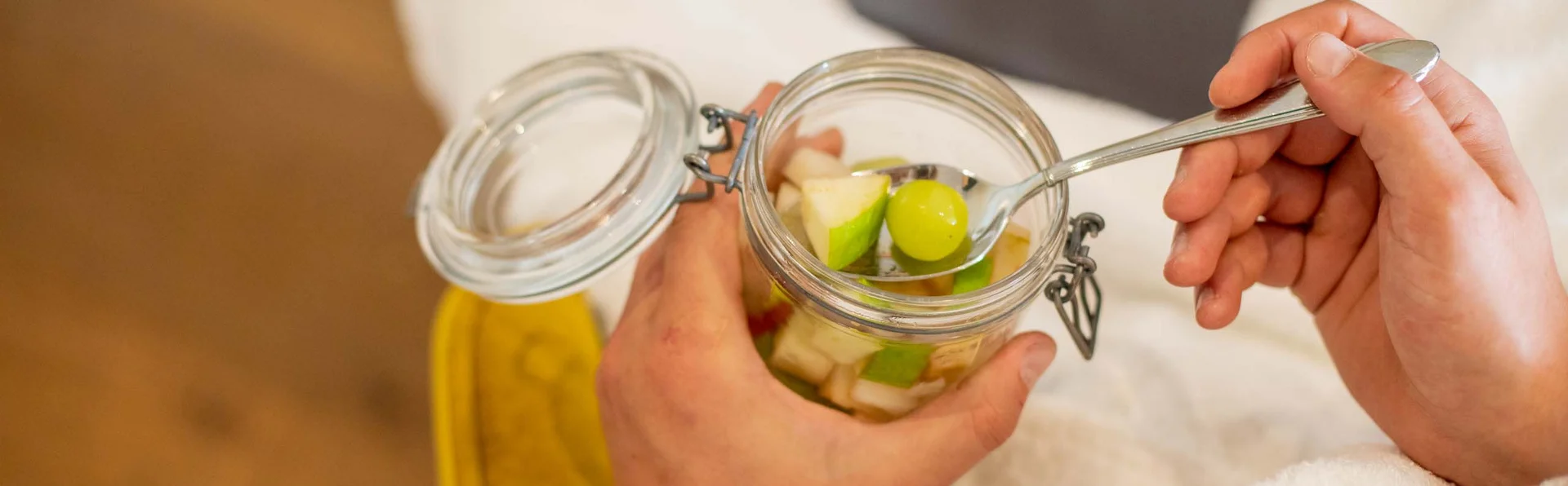 Gesund und vital im Fasten-Urlaub Person hält Glas mit Obstsalat und löffelt Trauben heraus