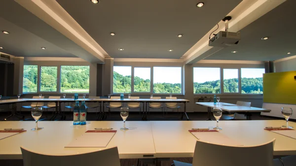 Moderner Konferenzraum mit Tischen, Stühlen und Deckenprojektor