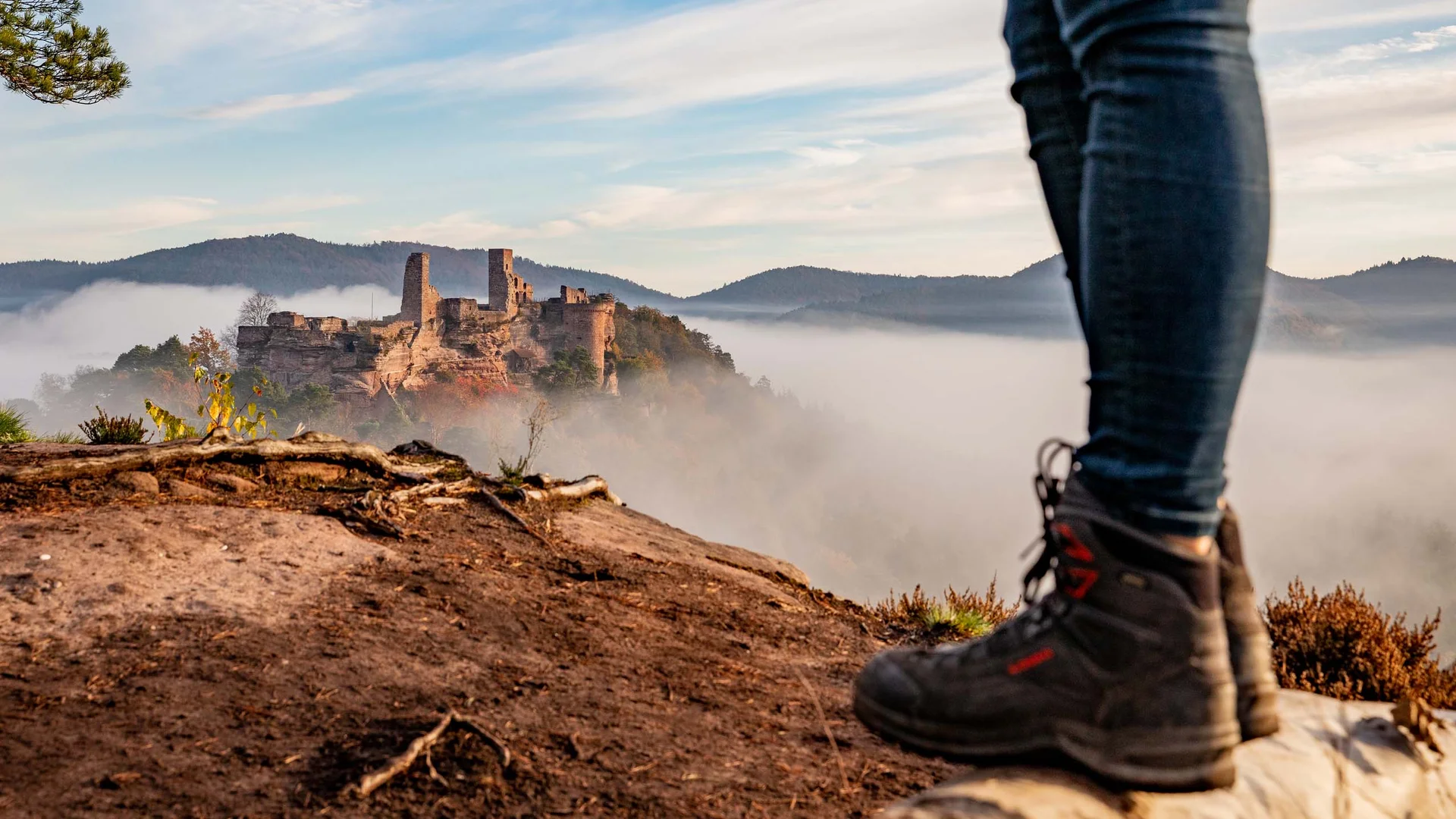 Wanderer blickt auf eine Burg in Nebel und Berge im Hintergrund