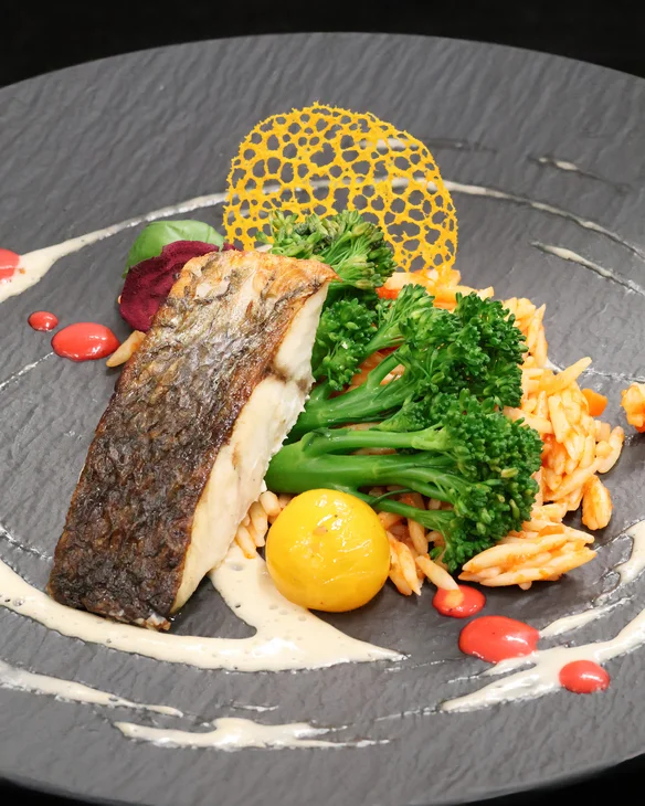 Gebratener Fisch mit Brokkoli, Reis und dekorativer Soße auf schwarzem Teller