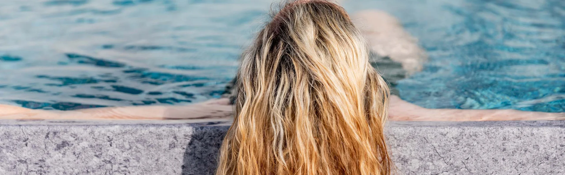 Frau mit langen, nassen Haaren lehnt am Poolrand