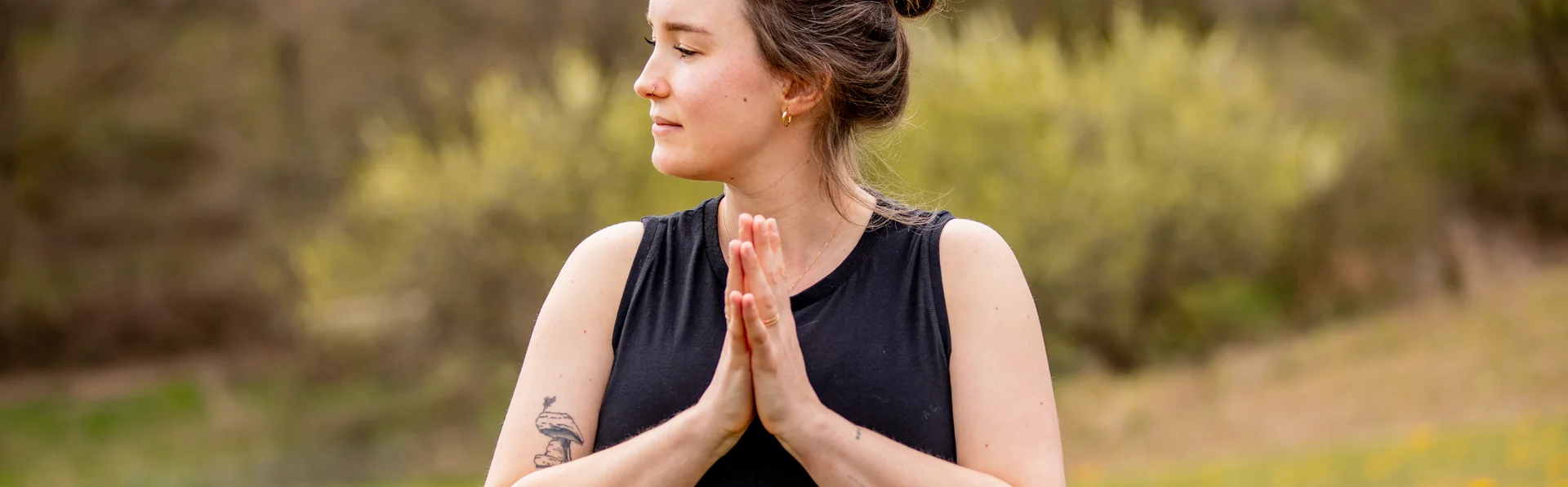 Autorin: Dorothee Leßmeister Frau in schwarzem Shirt meditiert draußen mit gefalteten Händen