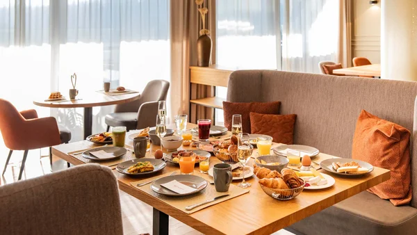 Gemütlicher Frühstückstisch mit vielfältigen Speisen und Getränken in einem hellen Restaurant