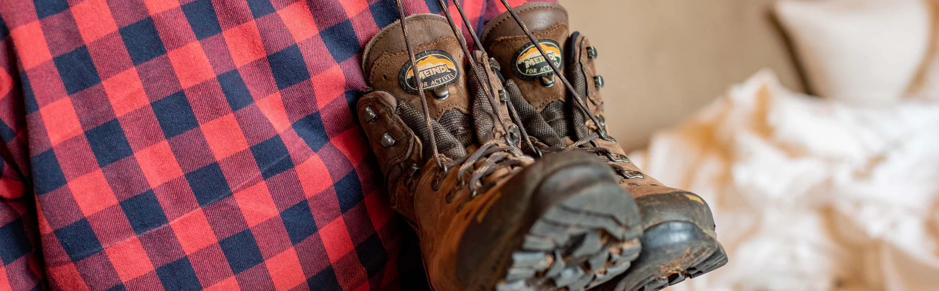 Wanderschuhe hängen über der Schulter einer Person mit rotem Karohemd