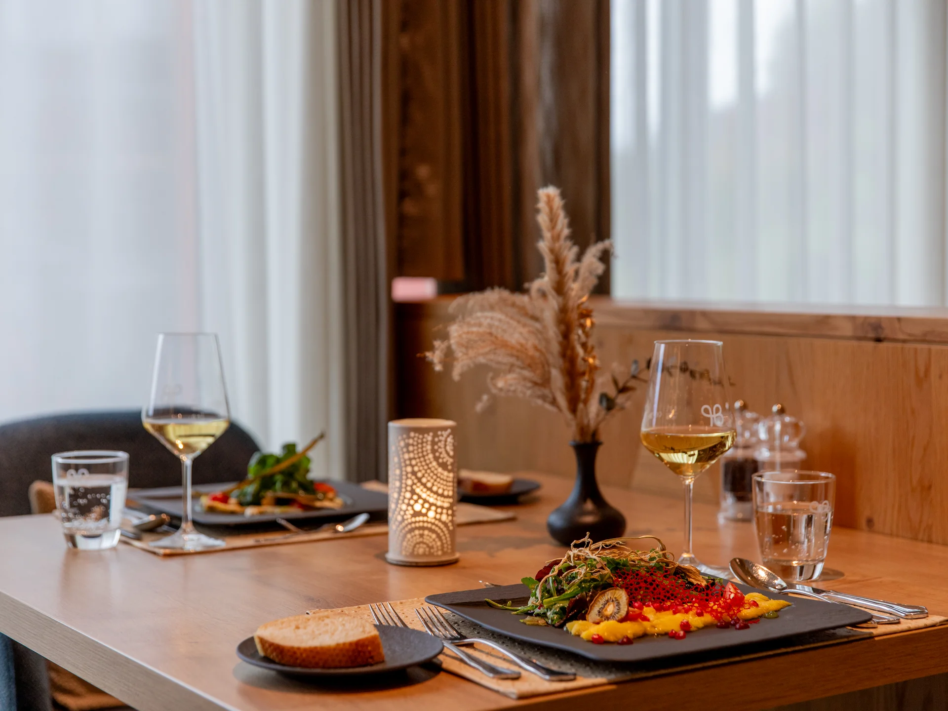 Gemütlicher Essensplatz mit Teller, Wein, Kerze und Deko auf Holztisch