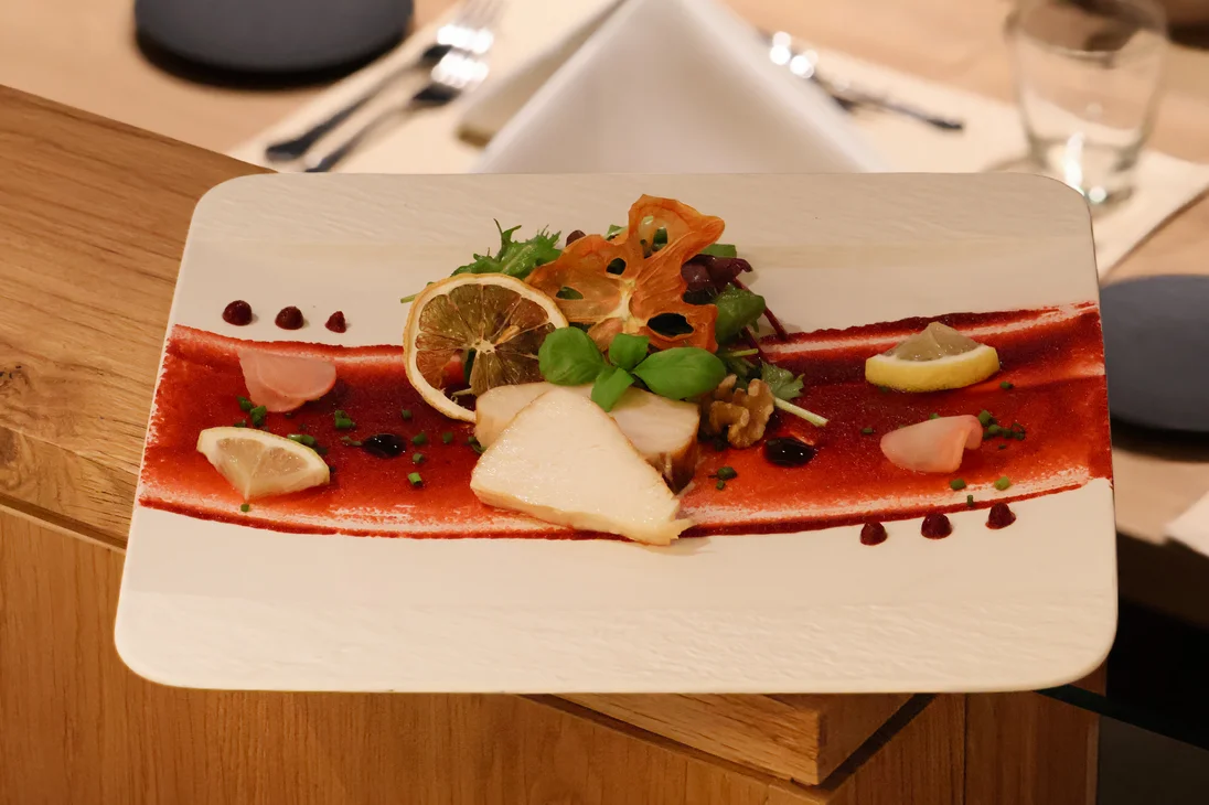 Kunstvoll angerichteter Fisch mit Salat, Zitronenscheiben und Soßendekoration auf weißem Teller