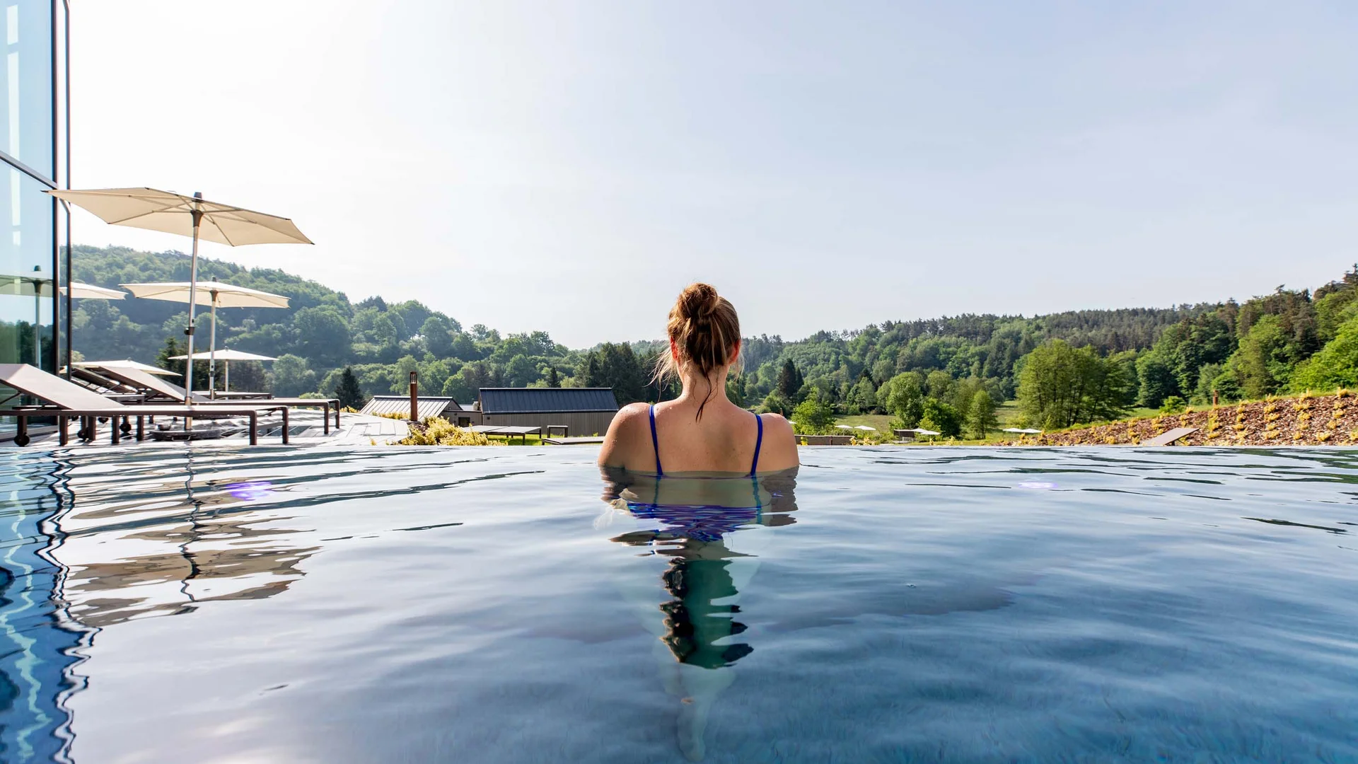 Femme se détendant dans une piscine avec vue sur collines boisées et parasols