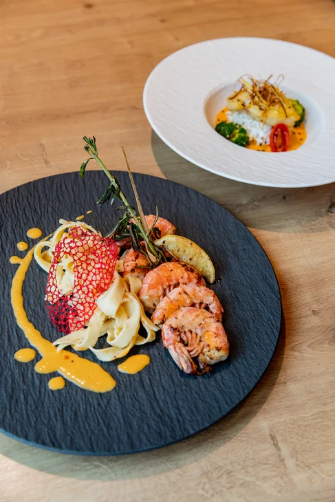 Garnelen mit Bandnudeln und Sauce auf schwarzem Teller, feine Garnitur auf Holztisch