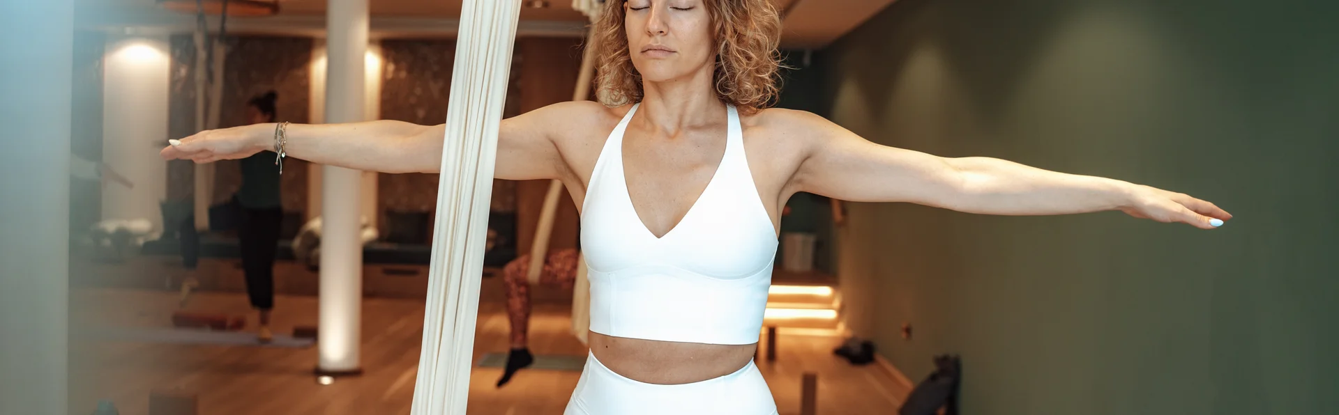 Leichtigkeit, Entspannung und Longevity Frau praktiziert Aerial Yoga mit Tuch in modernem Yoga-Studio