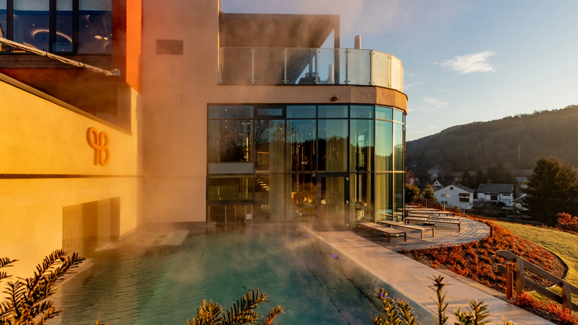 Dampfende Poollandschaft neben modernem Gebäude bei Sonnenuntergang