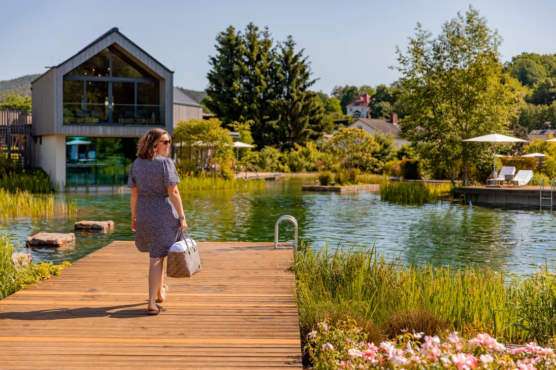 Ihr Hotel im Dahner Felsenland: Pfalzblick Wald Spa Resort Frau geht auf Steg am natürlichen Schwimmteich bei sonnigem Wetter