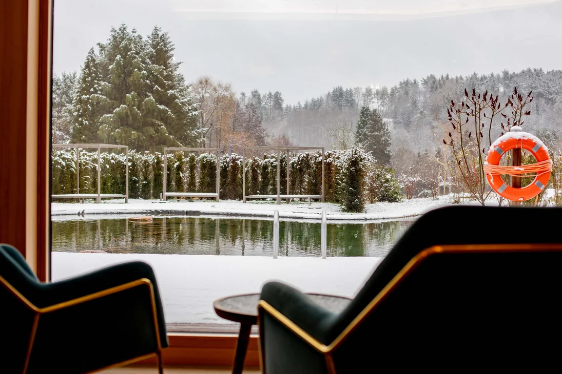 Blick aus Zimmer auf verschneiten Garten mit Teich und oranger Rettungsring