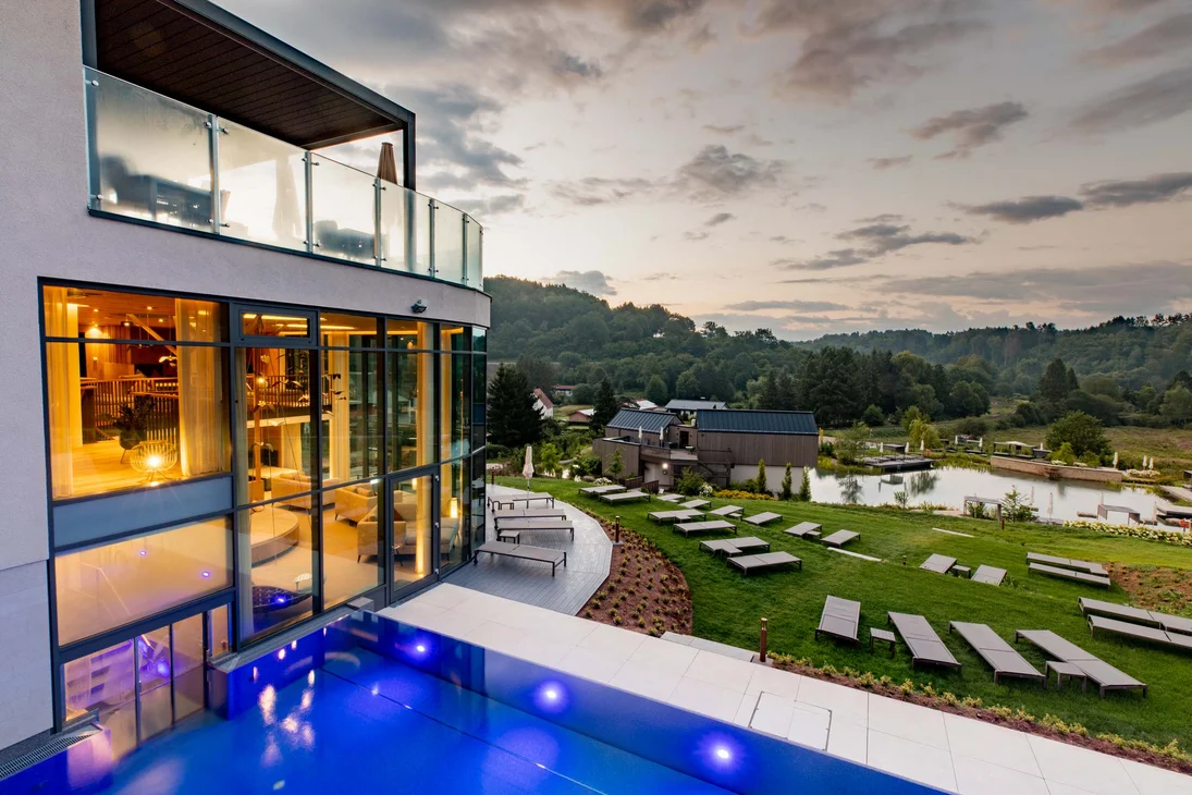 Hotel mit Außenpool, Liegestühlen und grüner Landschaft bei Sonnenuntergang