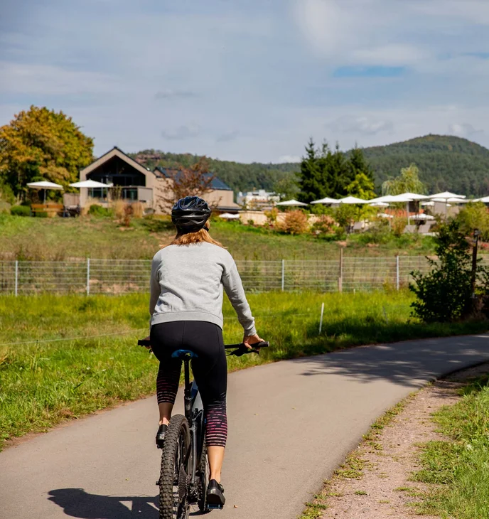 Frau fährt Fahrrad auf Landstraße mit Bergen und Häusern im Hintergrund