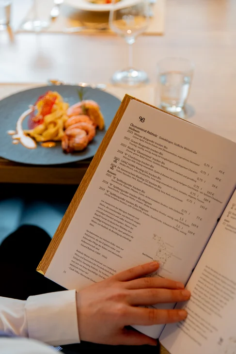 Person hält Weinliste mit Gericht und Glas Wasser auf dem Tisch