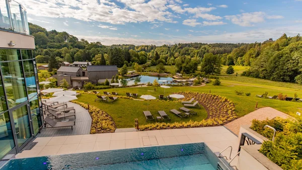 Moderner Pool mit Liegestühlen und grüner Landschaft unter blauem Himmel