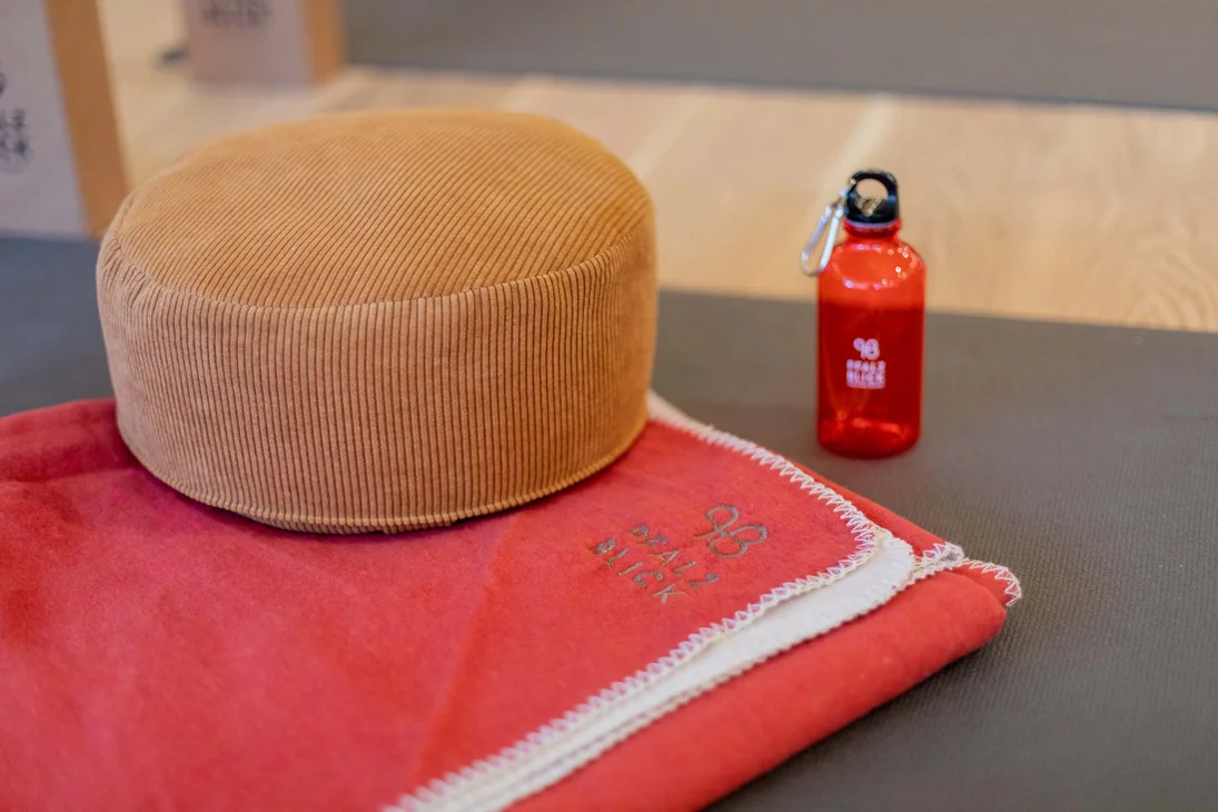 Beige Meditationskissen, rote Decke und rote Wasserflasche auf grauem Boden