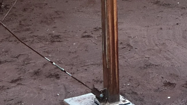 Poteau en bois fixé sur une dalle de béton dans la terre, avec des câbles de soutien