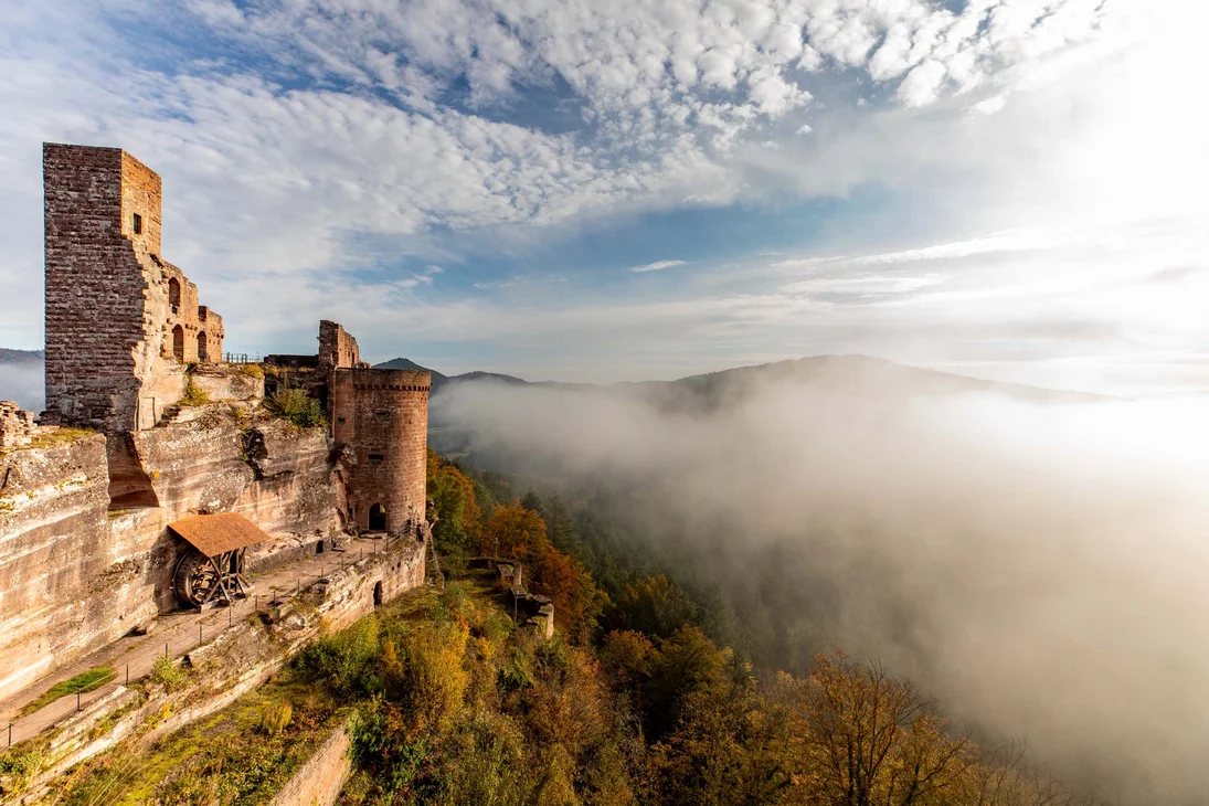 Burg auf felsigem Hügel mit Nebel und bewaldeten Hügeln im Hintergrund