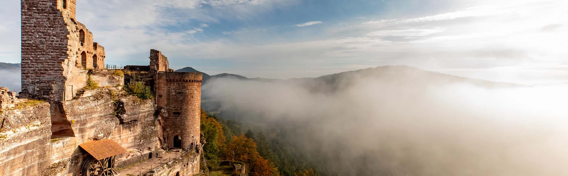 Burg auf felsigem Hügel mit Nebel und bewaldeten Hügeln im Hintergrund