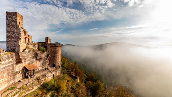 Burg auf felsigem Hügel mit Nebel und bewaldeten Hügeln im Hintergrund