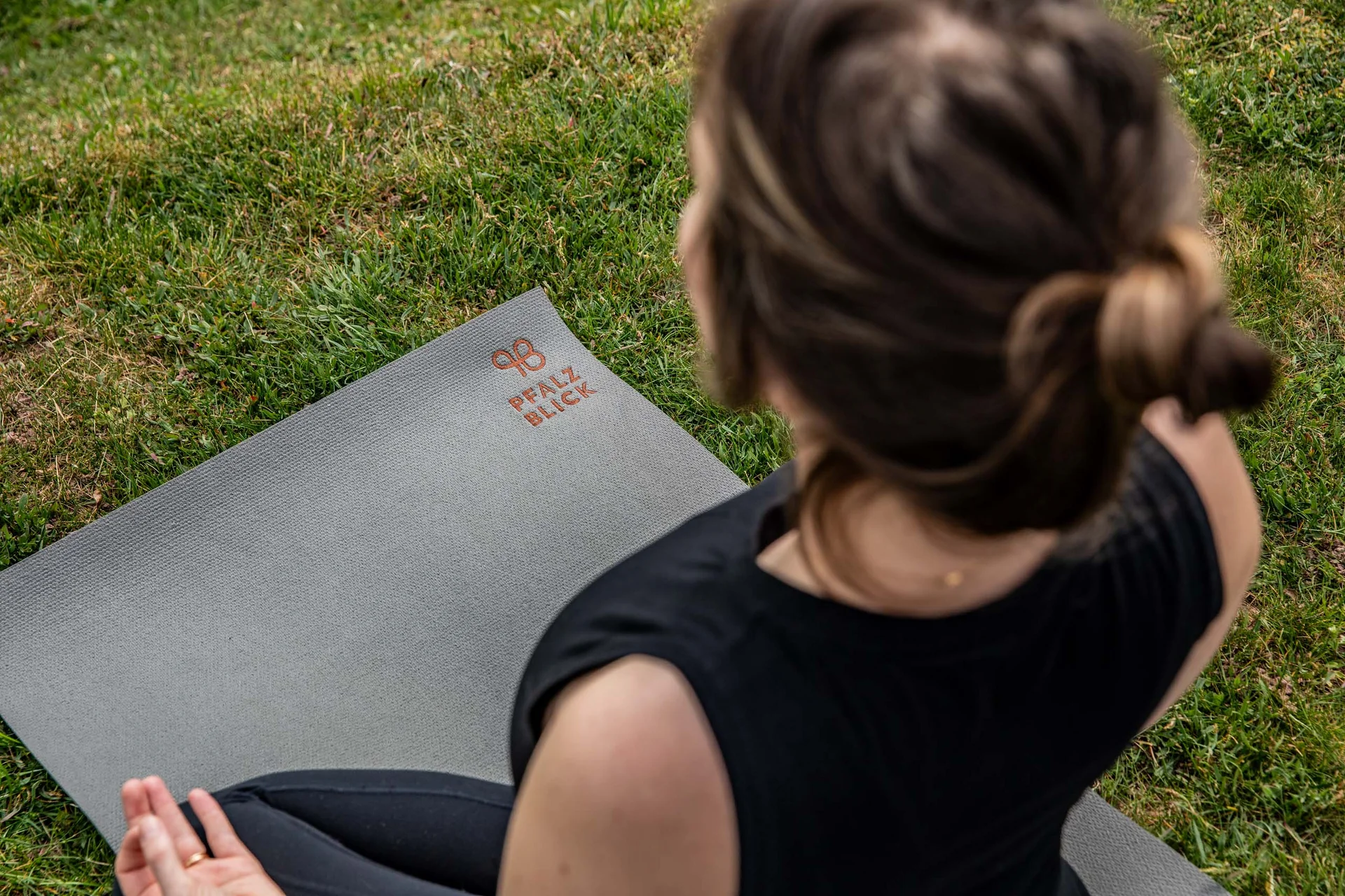 Frau meditiert im Schneidersitz auf Yogamatte im Freien auf Gras